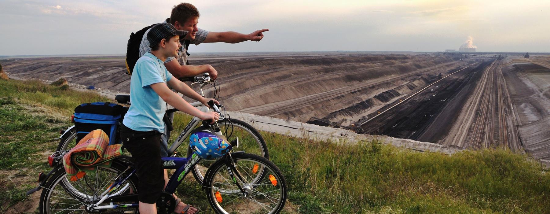 Vater und Sohn blicken vom Fahrrad in den Tagebau 
